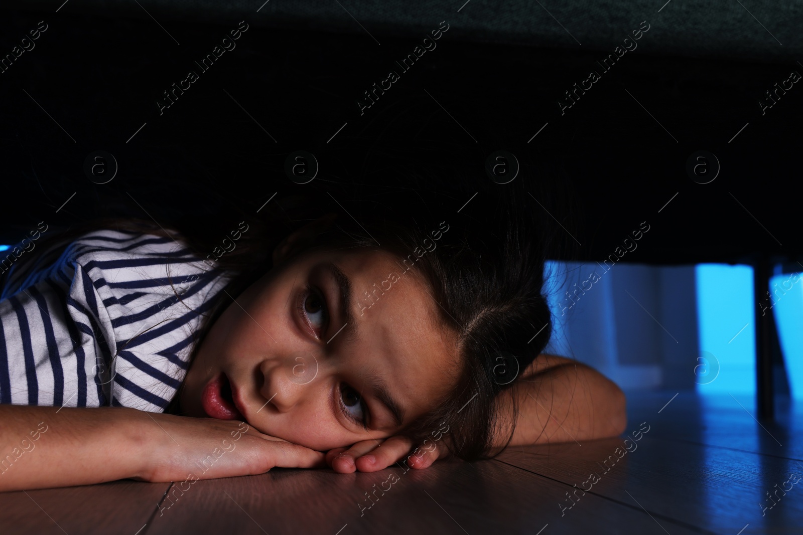 Photo of Fearful girl hiding under bed at night