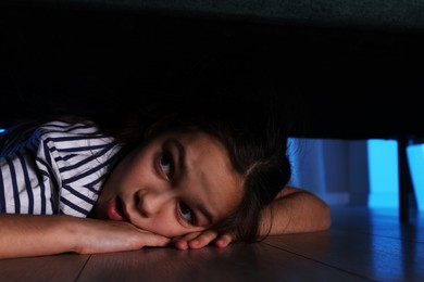 Photo of Fearful girl hiding under bed at night