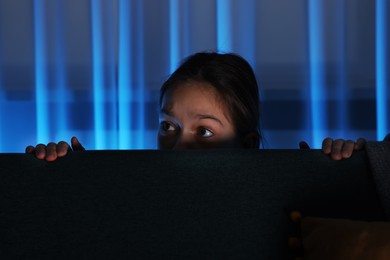 Scared girl hiding behind sofa at night