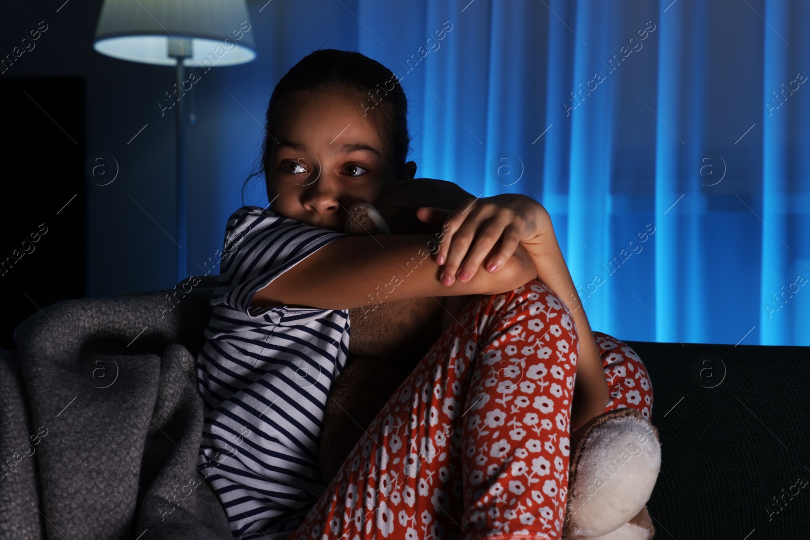 Photo of Afraid girl with teddy bear on sofa at home