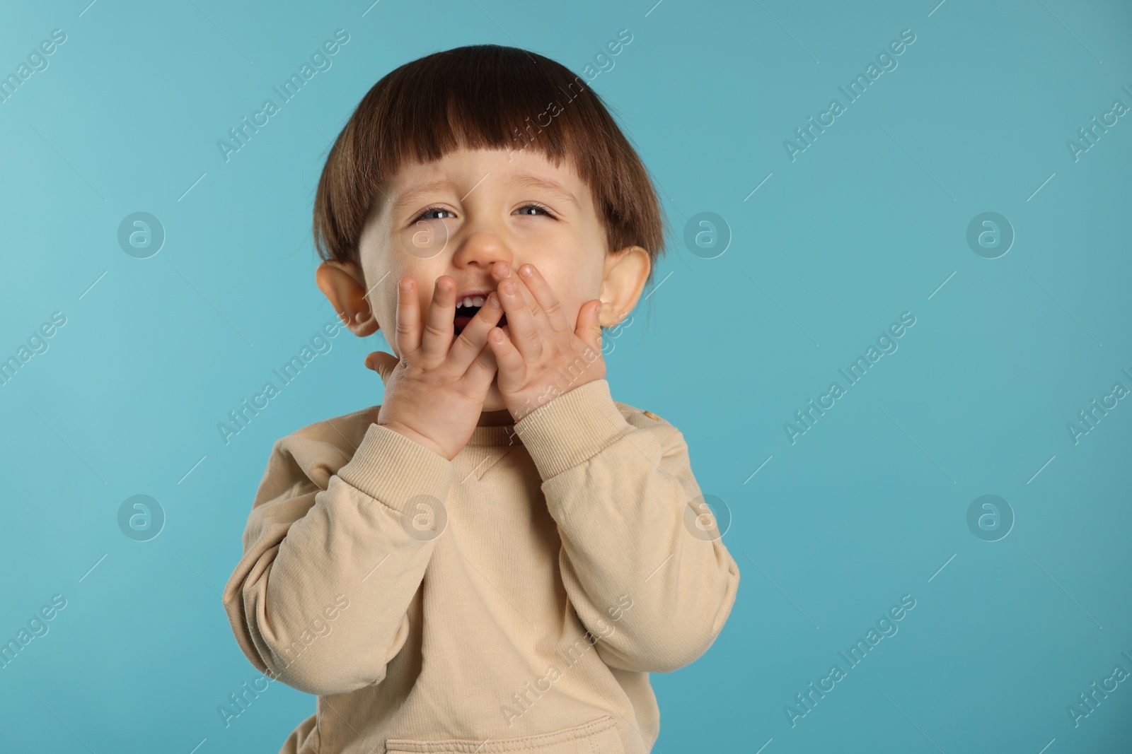 Photo of Portrait of emotional little boy covering mouth on light blue background. Space for text