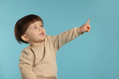 Photo of Portrait of cute little boy pointing at something on light blue background. Space for text