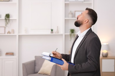 Photo of Real estate appraisal. Inspector with clipboard conducting property valuation indoors, space for text