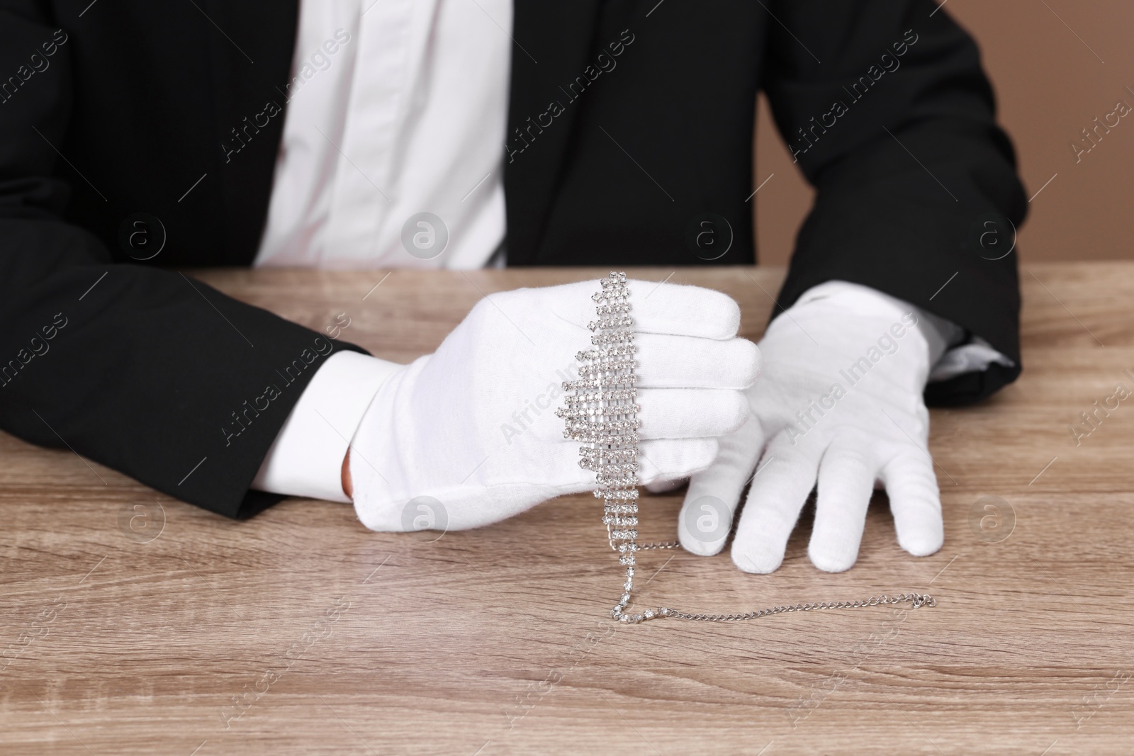 Photo of Appraiser in gloves with luxury necklace at wooden table, closeup