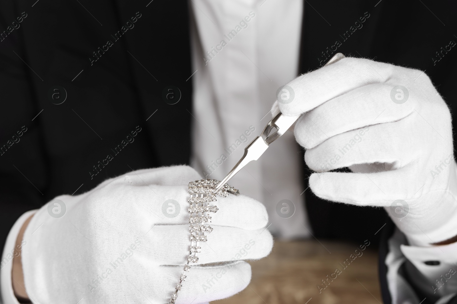 Photo of Appraiser with tweezers evaluating luxury necklace, closeup