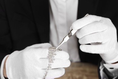 Photo of Appraiser with tweezers evaluating luxury necklace, closeup