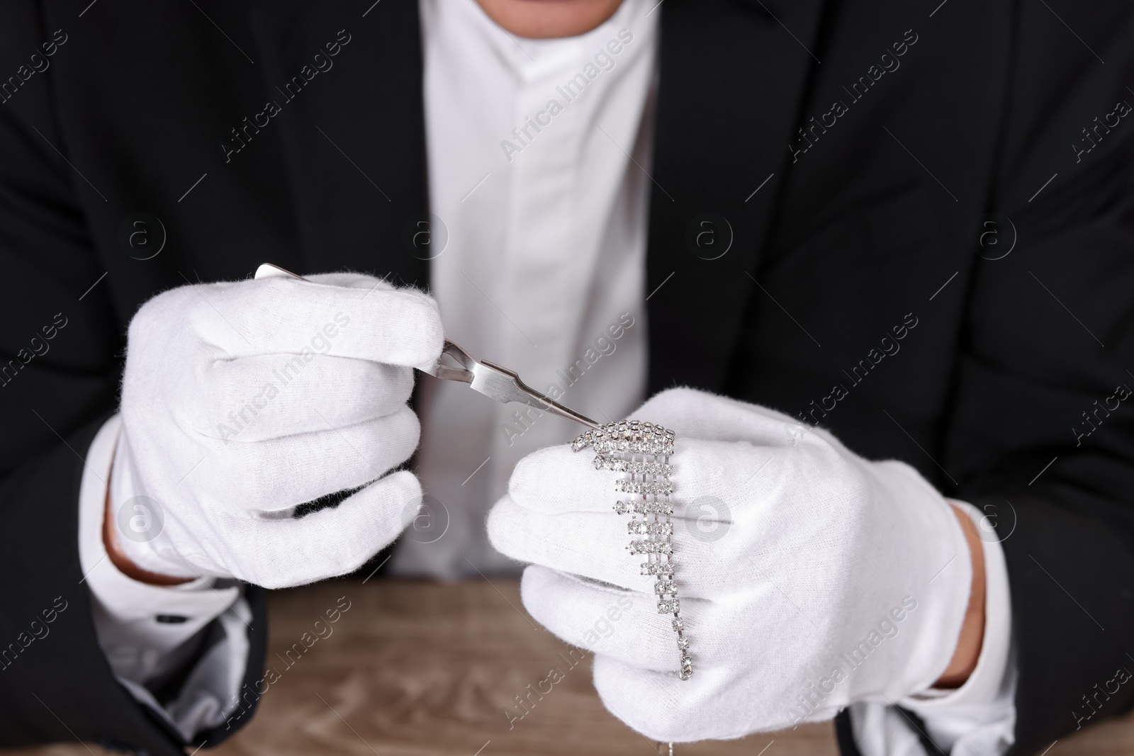 Photo of Appraiser with tweezers evaluating luxury necklace at table, closeup