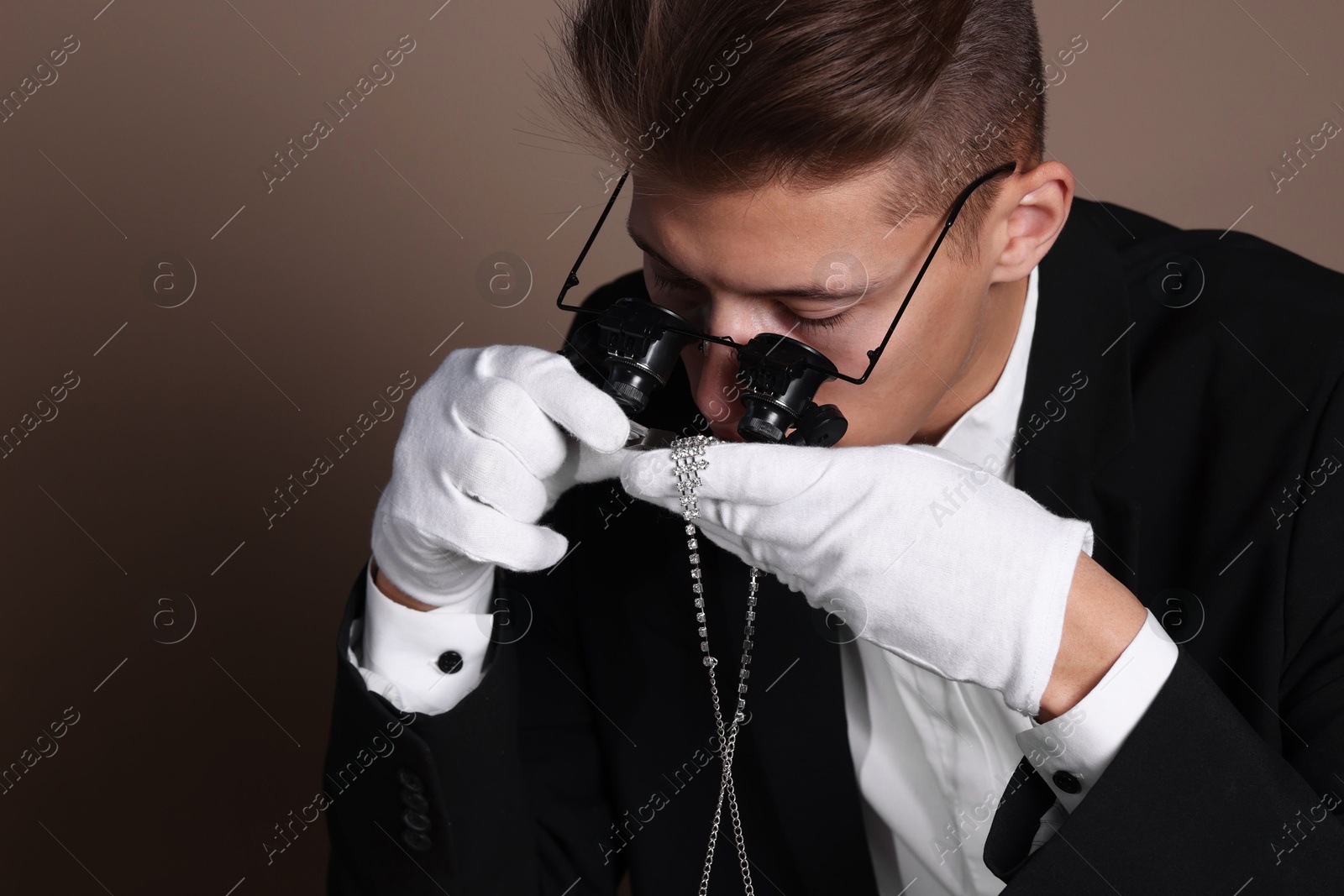 Photo of Appraiser with tweezers evaluating luxury necklace on brown background