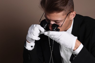 Photo of Appraiser with tweezers evaluating luxury necklace on brown background