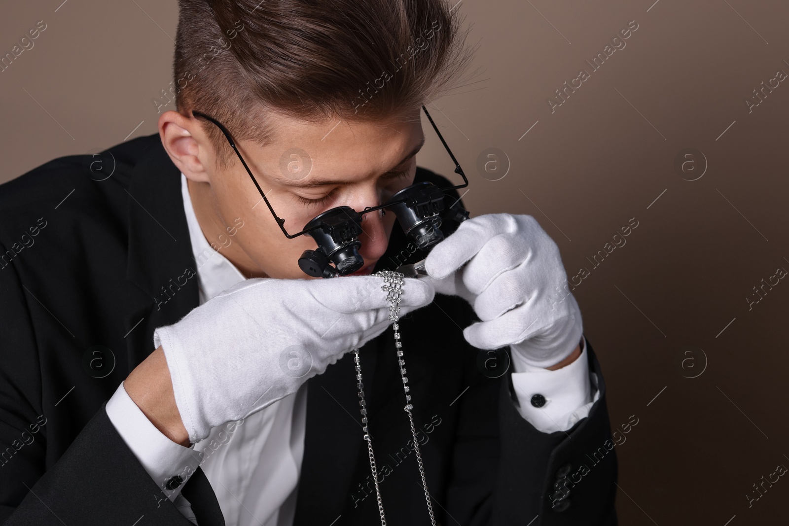 Photo of Appraiser with tweezers evaluating luxury necklace on brown background