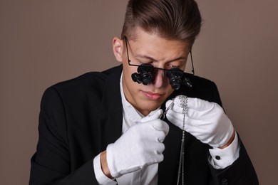 Photo of Appraiser with tweezers evaluating luxury necklace on brown background