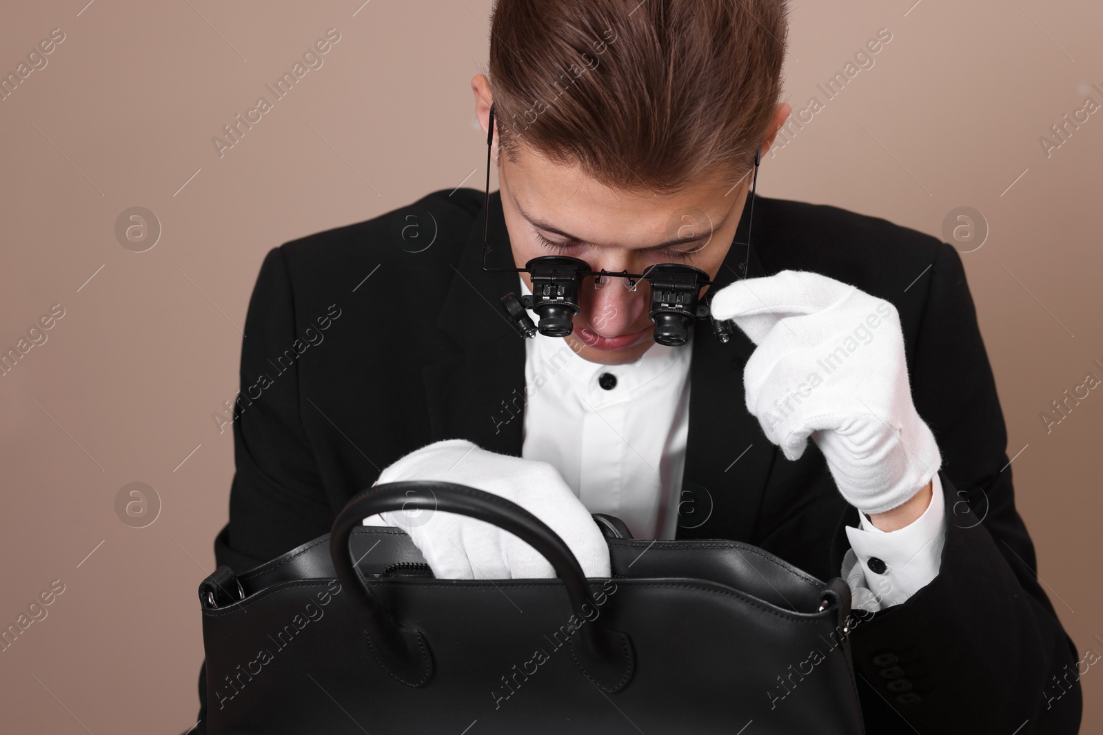 Photo of Appraiser evaluating leather bag on beige background