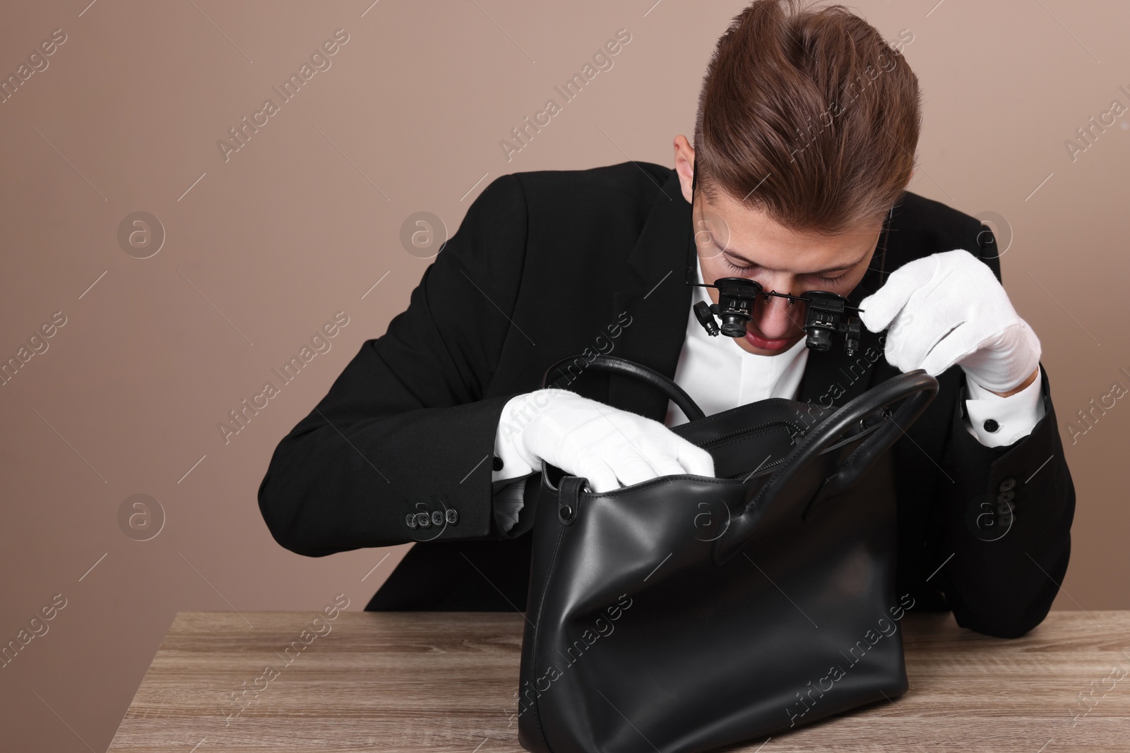 Photo of Appraiser evaluating leather bag at wooden table against beige background