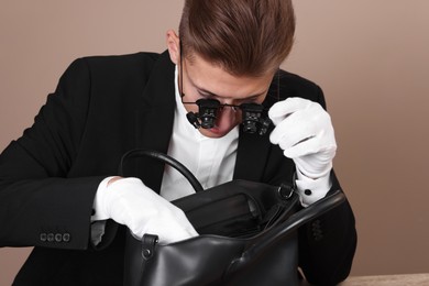 Photo of Appraiser evaluating leather bag on beige background