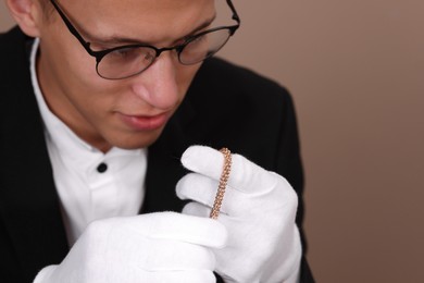 Photo of Appraiser evaluating luxury jewelry on beige background, closeup