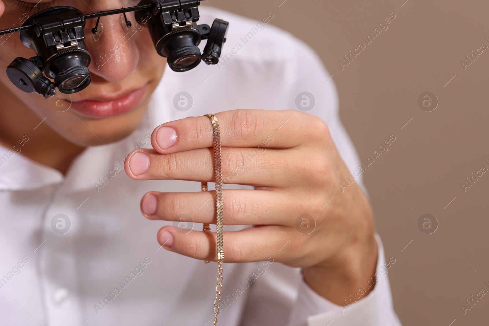 Photo of Appraiser evaluating luxury jewelry on beige background, closeup. Space for text