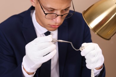 Photo of Appraiser with tweezers evaluating luxury jewelry on beige background