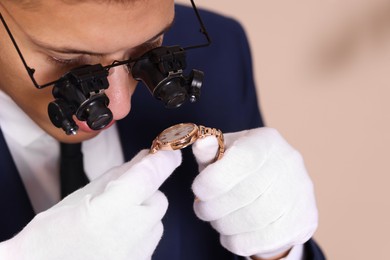 Photo of Appraiser evaluating luxury wristwatch on beige background, closeup