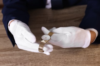 Photo of Appraiser with luxury wristwatch at wooden table, closeup