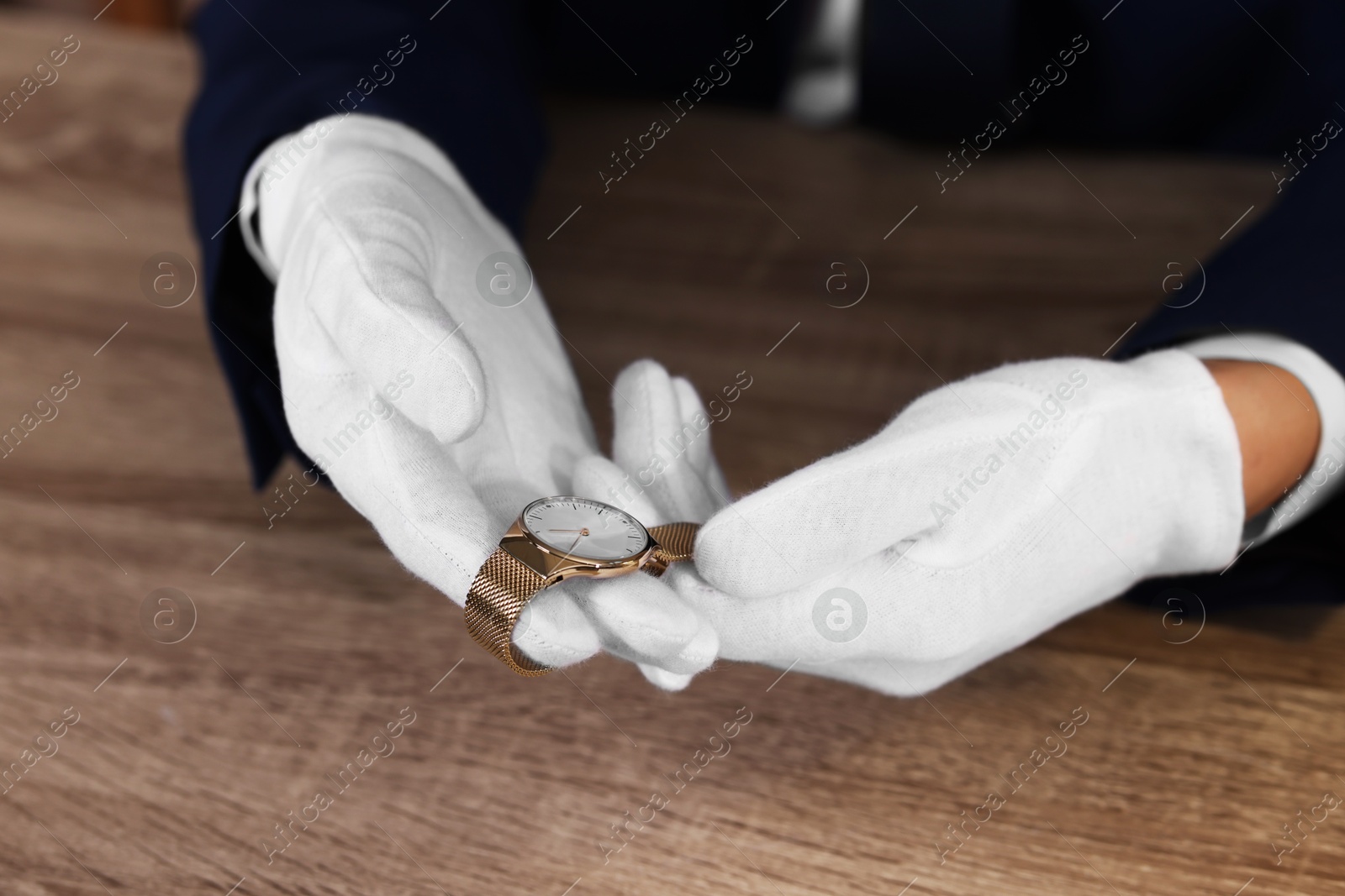 Photo of Appraiser with luxury wristwatch at wooden table, closeup