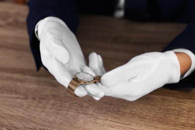 Photo of Appraiser with luxury wristwatch at wooden table, closeup