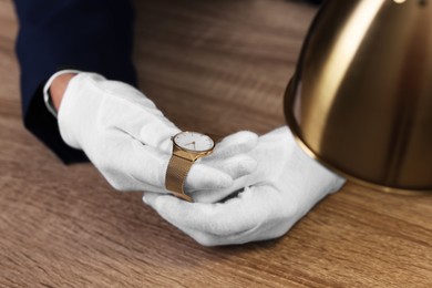 Photo of Appraiser with luxury wristwatch at wooden table, closeup