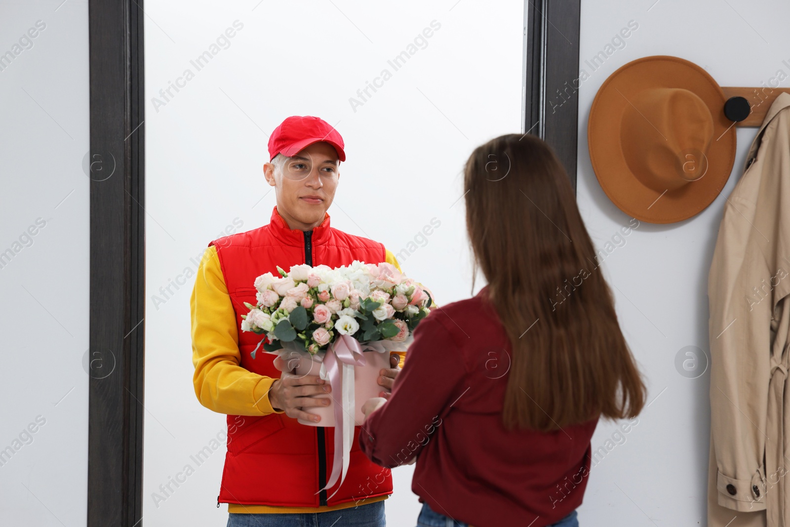 Photo of Happy delivery man giving gift box with beautiful floral composition to woman at door