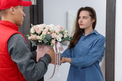 Photo of Woman receiving gift box with beautiful floral composition from delivery man at door