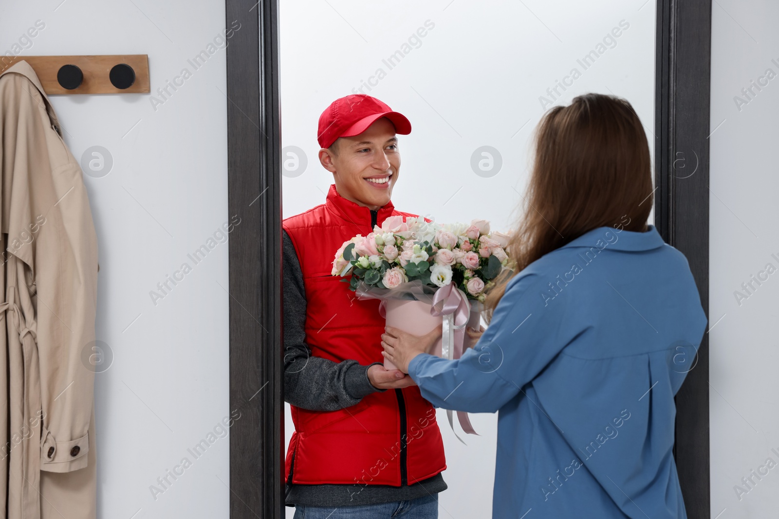 Photo of Smiling delivery man giving gift box with beautiful floral composition to woman at door