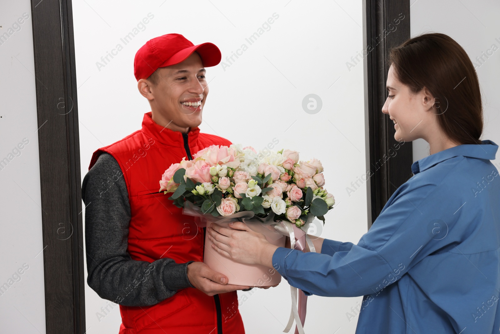 Photo of Smiling delivery man giving gift box with beautiful floral composition to woman at door