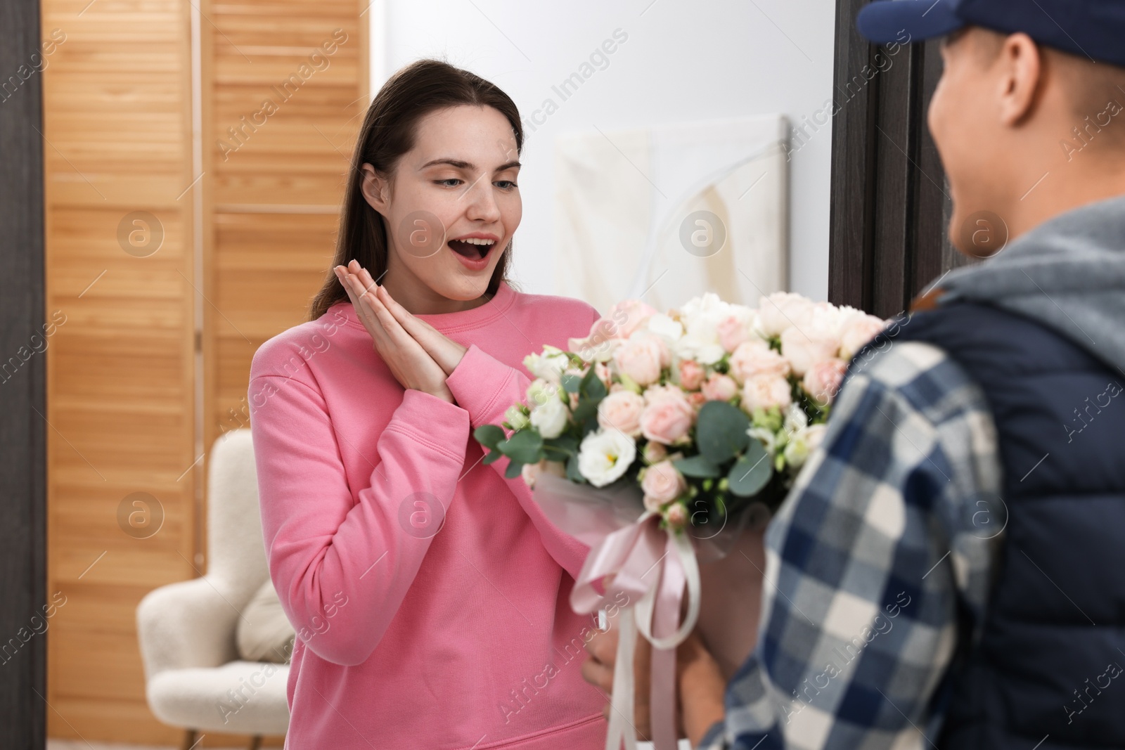 Photo of Surprised woman receiving gift box with beautiful floral composition from delivery man at door