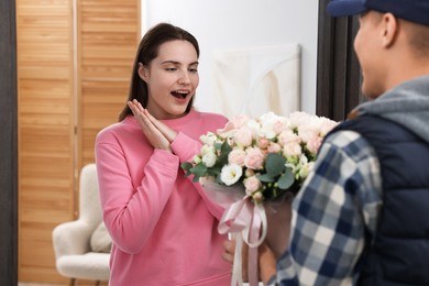 Photo of Surprised woman receiving gift box with beautiful floral composition from delivery man at door