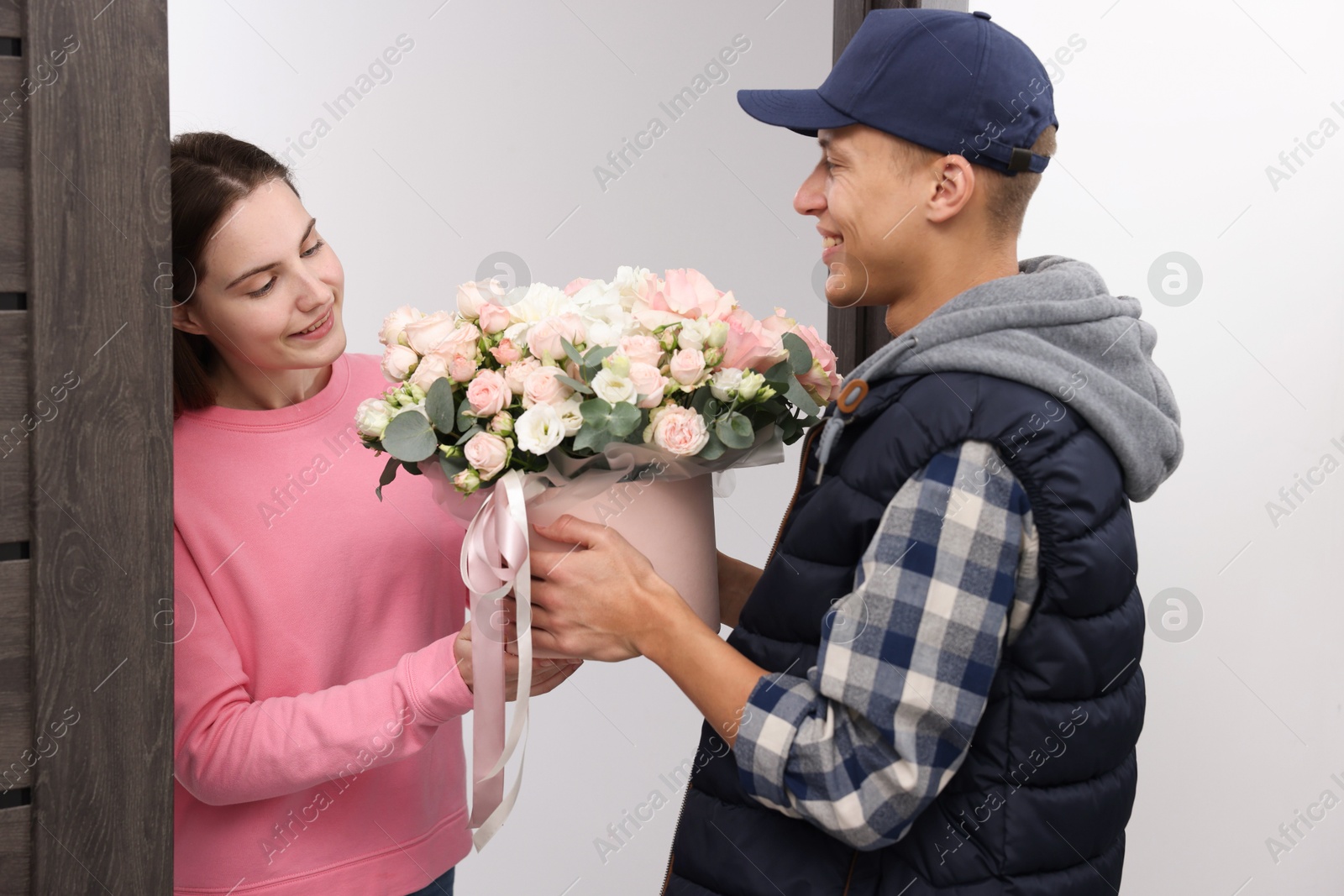 Photo of Happy woman receiving gift box with beautiful floral composition from delivery man at door