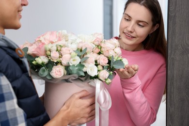 Photo of Happy woman receiving gift box with beautiful floral composition from delivery man at door