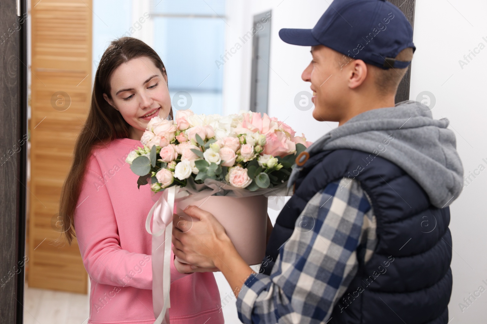 Photo of Happy woman receiving gift box with beautiful floral composition from delivery man at door