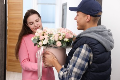 Happy woman receiving gift box with beautiful floral composition from delivery man at door