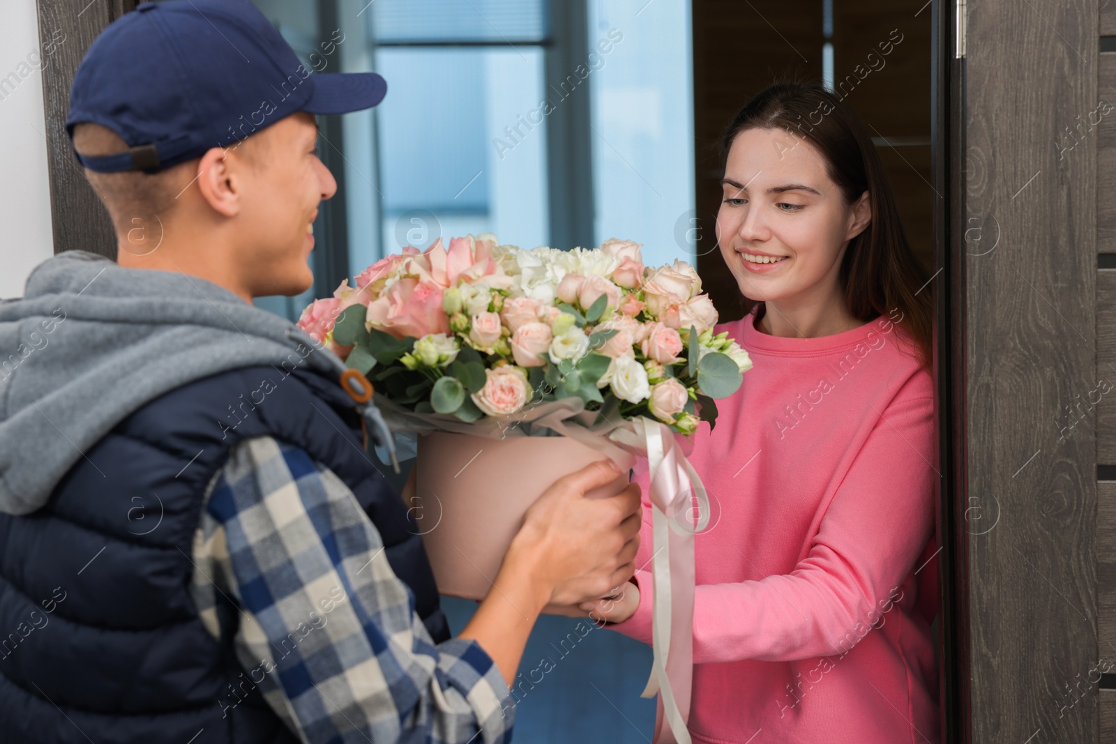 Photo of Happy woman receiving gift box with beautiful floral composition from delivery man at door