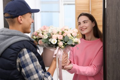 Photo of Happy woman receiving gift box with beautiful floral composition from delivery man at door