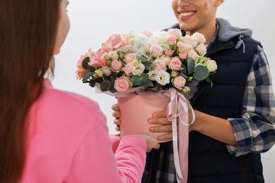 Photo of Happy delivery man giving gift box with beautiful floral composition to woman on white background, closeup