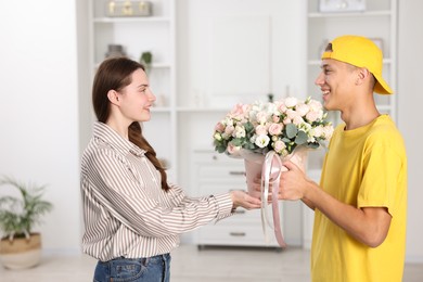 Photo of Happy delivery man giving gift box with beautiful floral composition to woman indoors