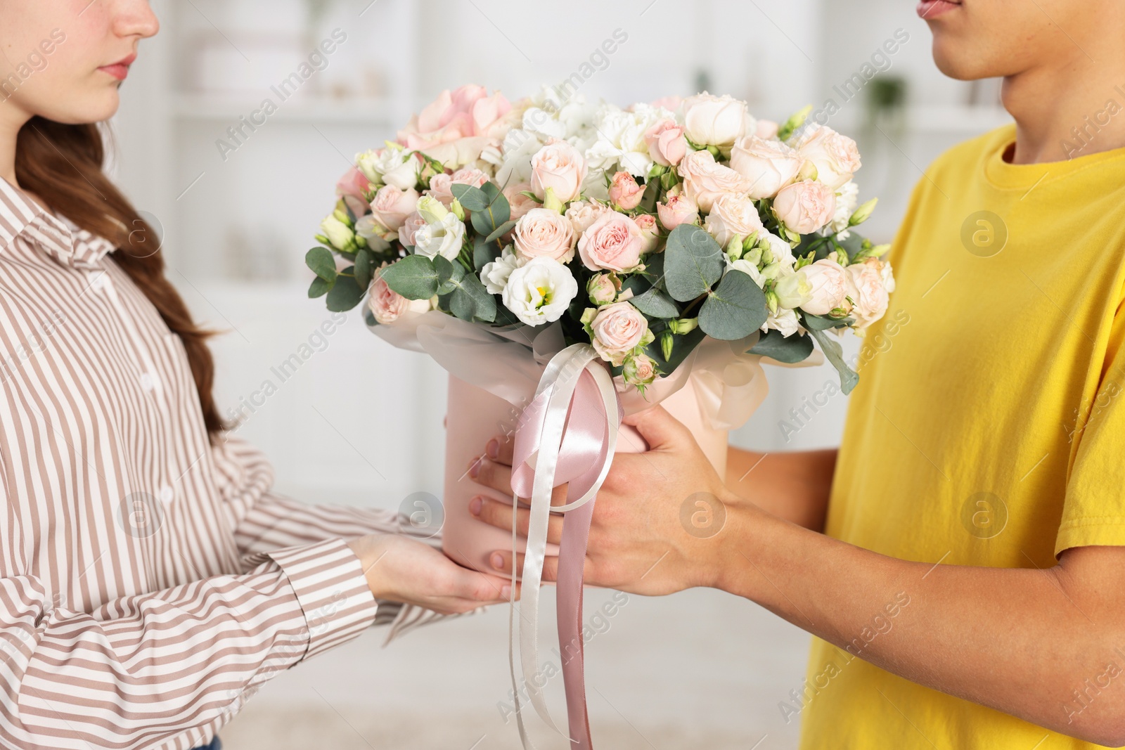 Photo of Delivery man giving gift box with beautiful floral composition to woman indoors, closeup