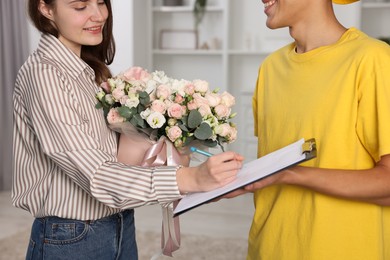 Photo of Smiling woman signing for delivered gift box with floral composition indoors, closeup