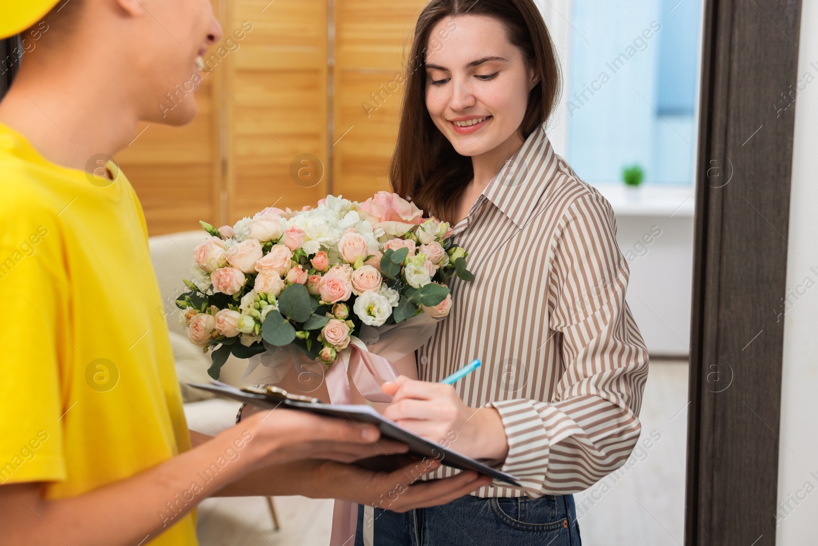 Photo of Smiling woman signing for delivered gift box with floral composition indoors, closeup