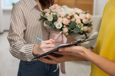 Photo of Woman signing for delivered gift box with floral composition indoors, closeup