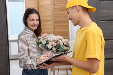 Photo of Smiling woman signing for delivered gift box with floral composition at door