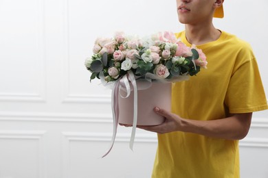 Photo of Delivery man holding gift box with beautiful floral composition near white wall, closeup. Space for text