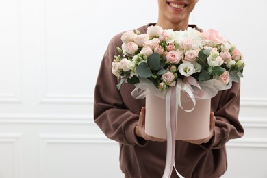 Photo of Smiling delivery man holding gift box with beautiful floral composition near white wall, closeup. Space for text