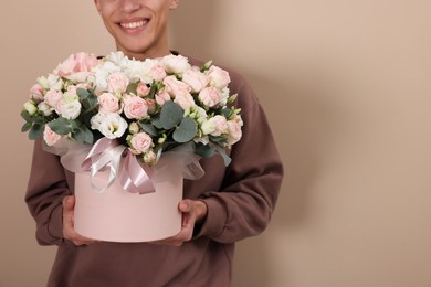 Photo of Smiling delivery man holding gift box with beautiful floral composition on beige background, closeup. Space for text