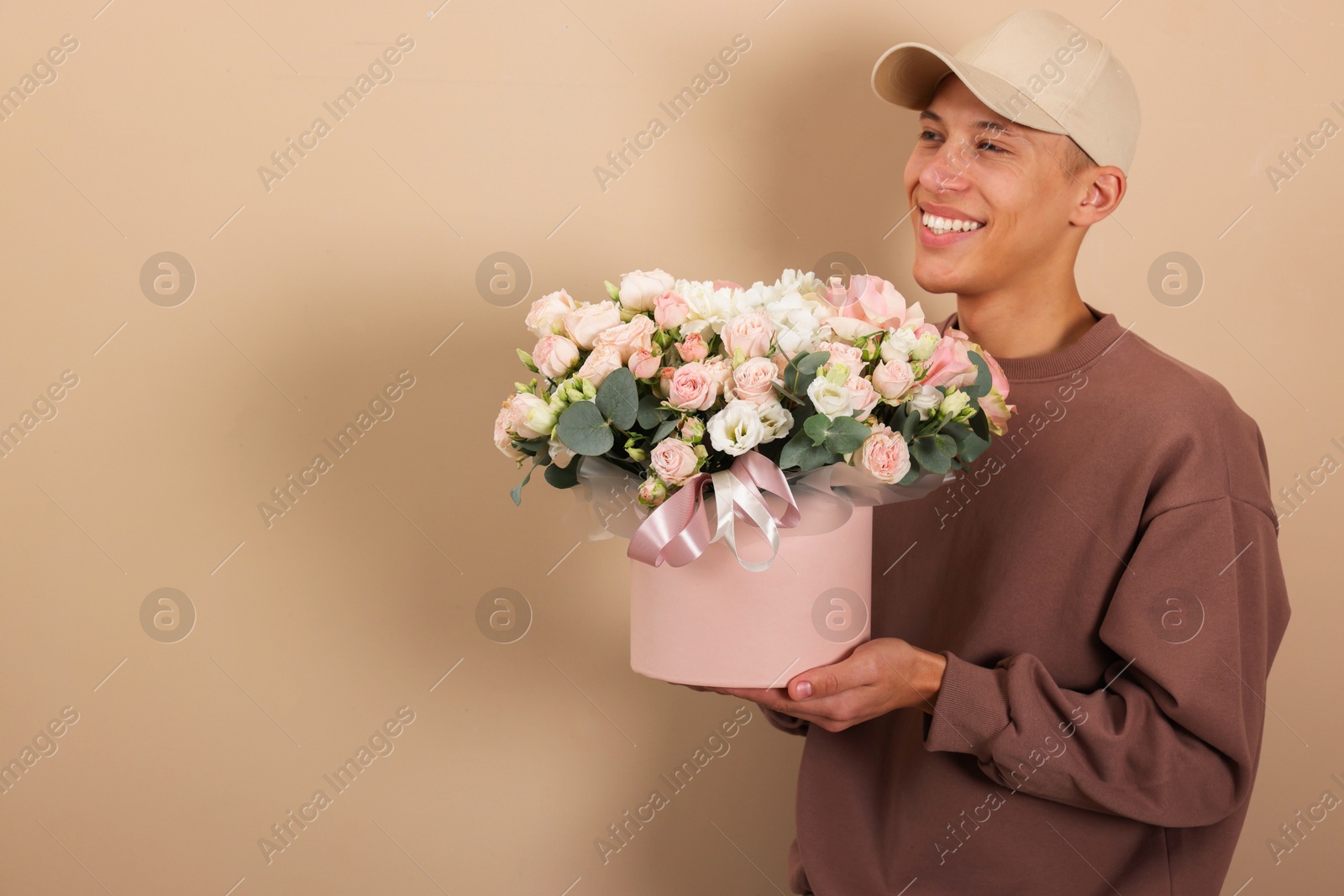 Photo of Smiling delivery man holding gift box with beautiful floral composition on beige background. Space for text