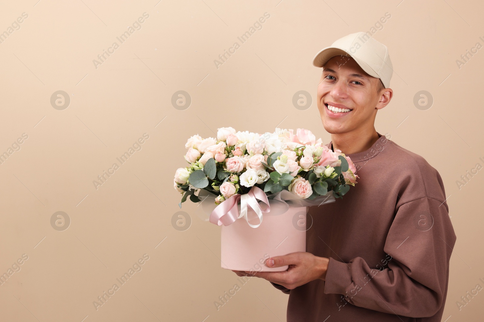 Photo of Smiling delivery man holding gift box with beautiful floral composition on beige background. Space for text